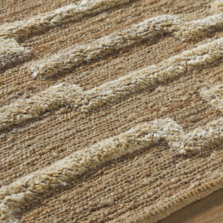 Close-up of the hand-woven Miya Area Rug. Natural jute rug with beige, tan, and brown hues and raised stripe pattern. Texture