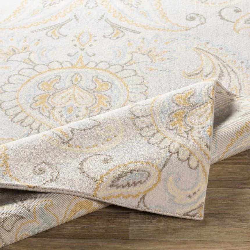 Close-up of Simpatico Candice Olson x LIVABLISS SPO-1001 rug. Cream wool rug with light blue, mustard, and ivory paisley pattern. Fold