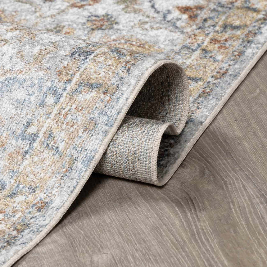 Close-up of the Dion Washable Floral Rug showing its charcoal, beige, and blue traditional pattern and soft texture. Fold