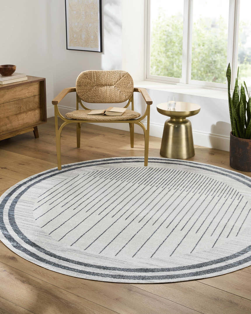 Living room scene with a round Thad Medium Gray Washable Area Rug, woven chair, wood dresser, and gold side table. Roomscene-Round