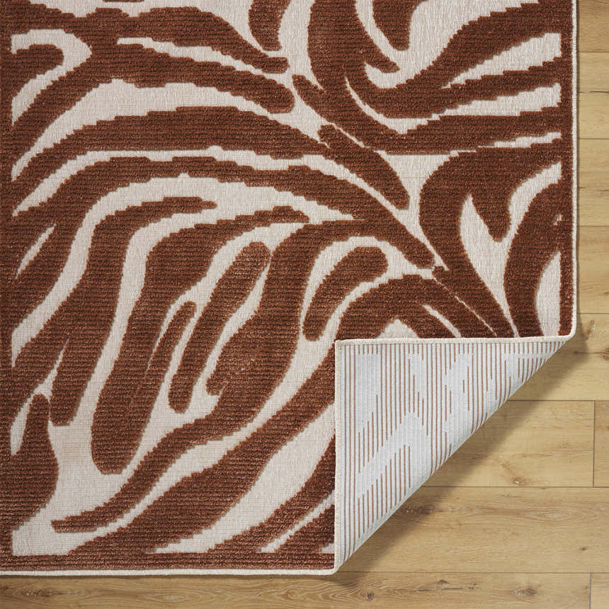 Close-up of Keto Brown Washable Area Rug with a brown and off-white abstract pattern on light wood floors. Fold