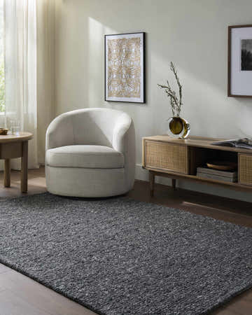Living room scene with a gray Sevan Charcoal Wool Area Rug, cream chair, and wood media console. Roomscene-Rectangle