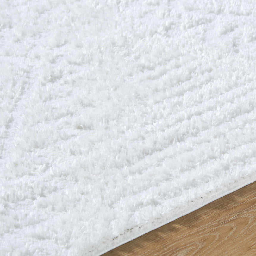 Close up of the plush texture of the Edsel Off-White Area Rug on hardwood floor. Texture