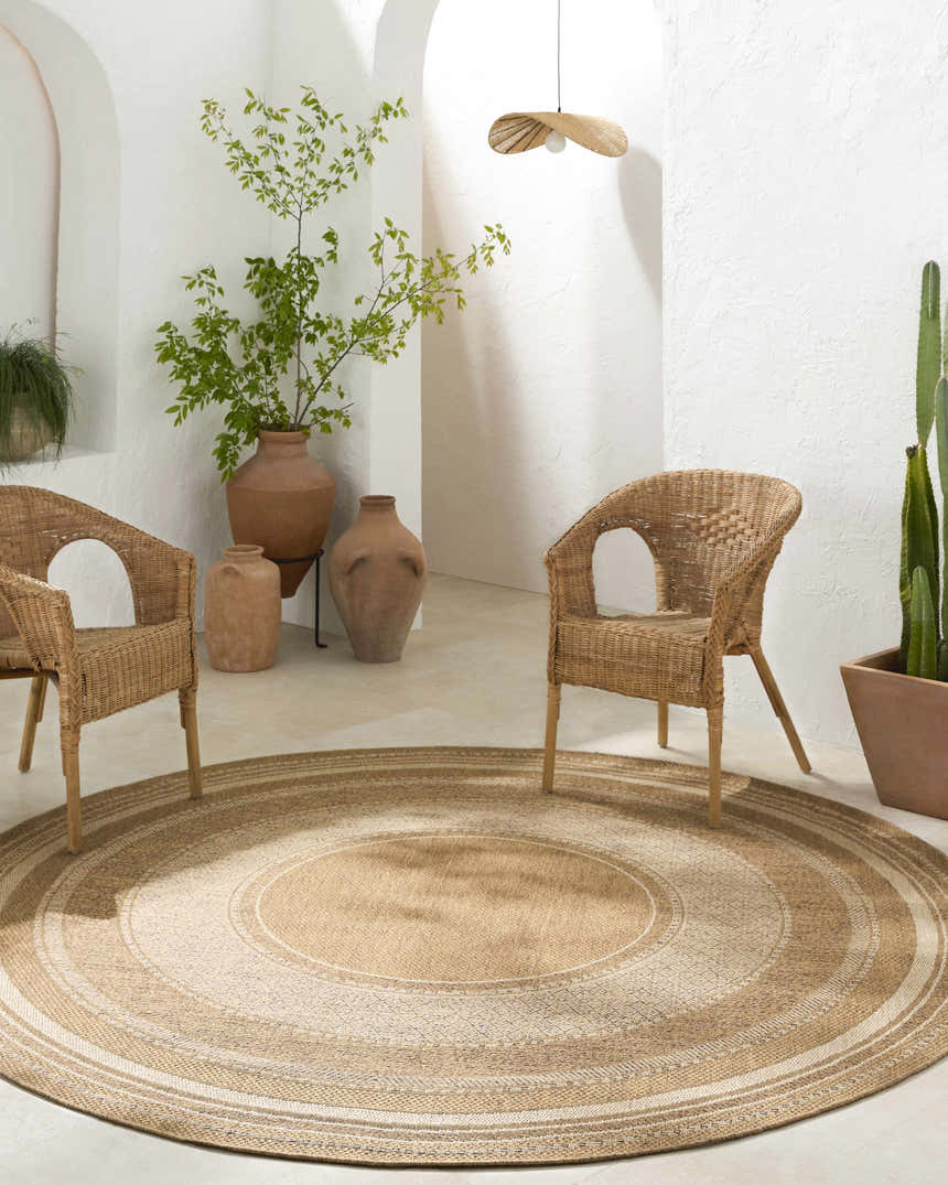 Boho-style room with a round Chael Flatweave Faux Jute Rug, wicker chairs, terracotta pots, and white textured walls. Roomscene-Round