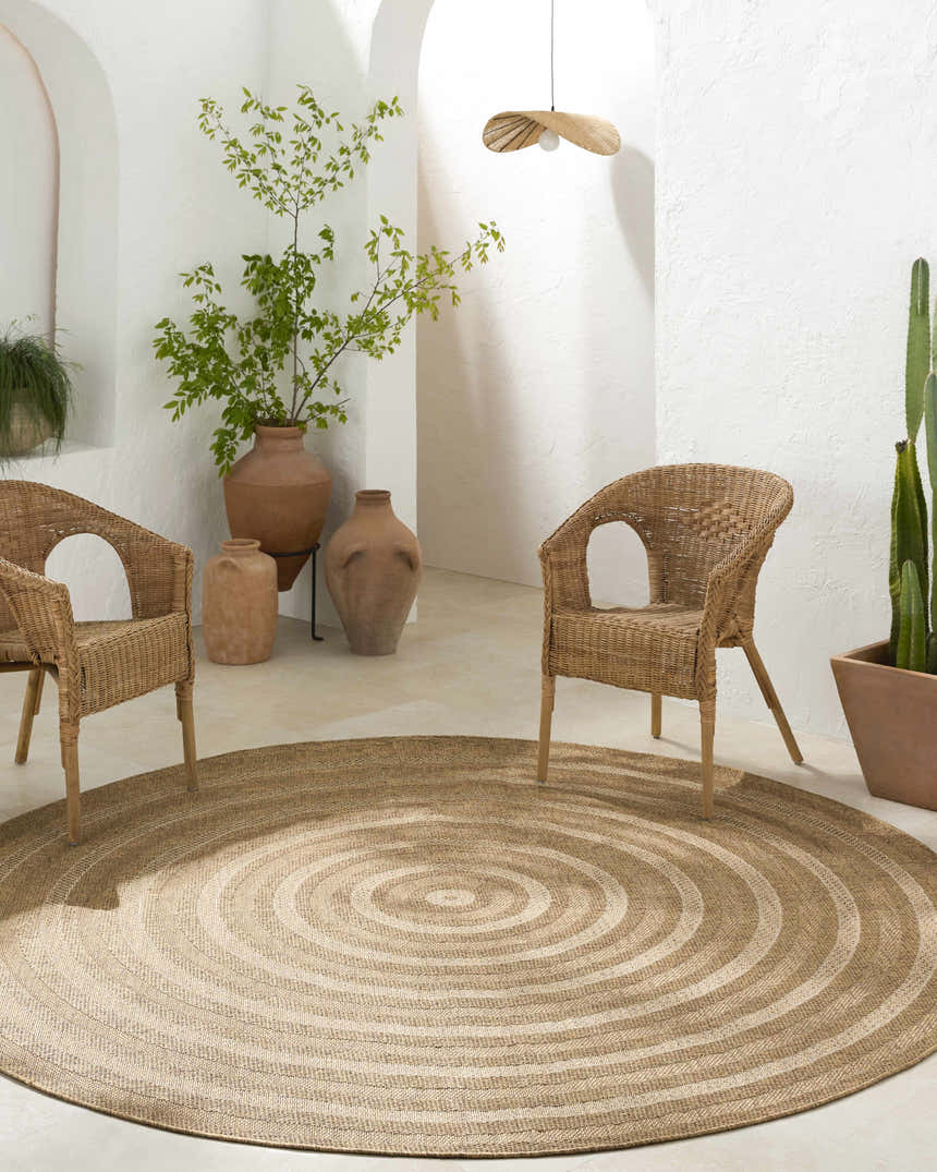Neutral room scene with wicker chairs and a round Dyami Flatweave Faux Jute Rug in a concentric circle pattern. Roomscene-Round
