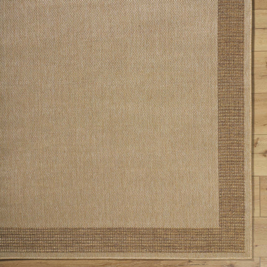 Close-up of the Inigo Flatweave Faux Jute Rug. Beige rug with a dark brown border on a wood floor. Corner