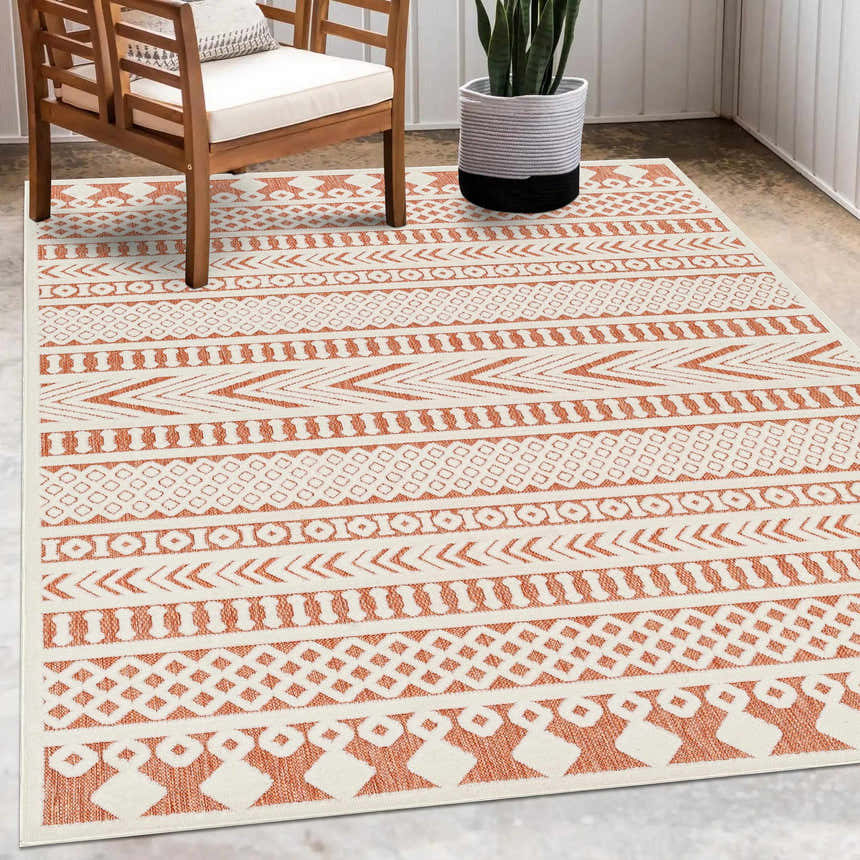 Outdoor patio scene with a Jove Orange rug, wooden chair, and potted snake plant. Roomscene-Rectangle