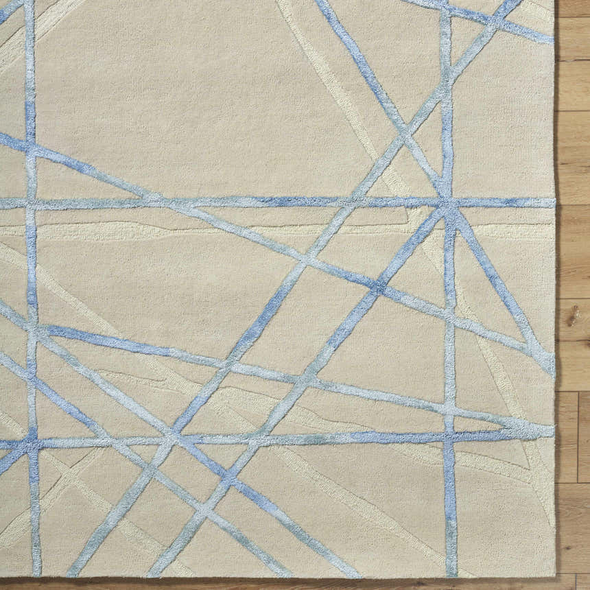 Close-up of the Hiba Area Rug showing a beige wool texture with a slate blue geometric line pattern. Corner