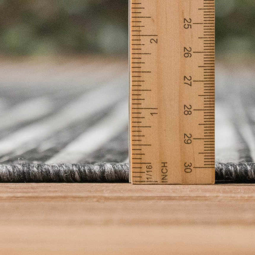 Close-up of the Stephan Area Rug showing pile height with a ruler. Colors are black, charcoal, cream, and light gray. Pile