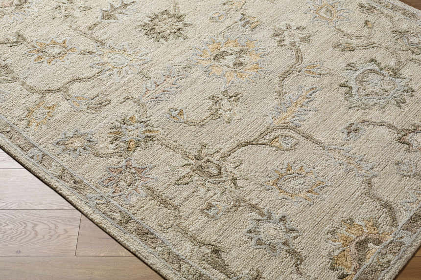 Close-up of the hand-tufted Adelle Tufted Oushak Area Rug. Beige wool rug with a traditional floral pattern in tan, beige, and brown. Corner
