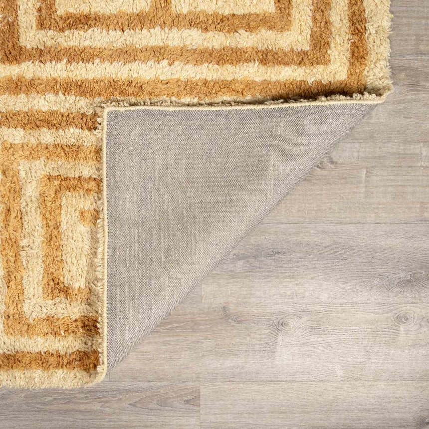 Close-up of the hand-tufted Wasim Area Rug showing its geometric brick red and tan pattern and wool texture. Fold