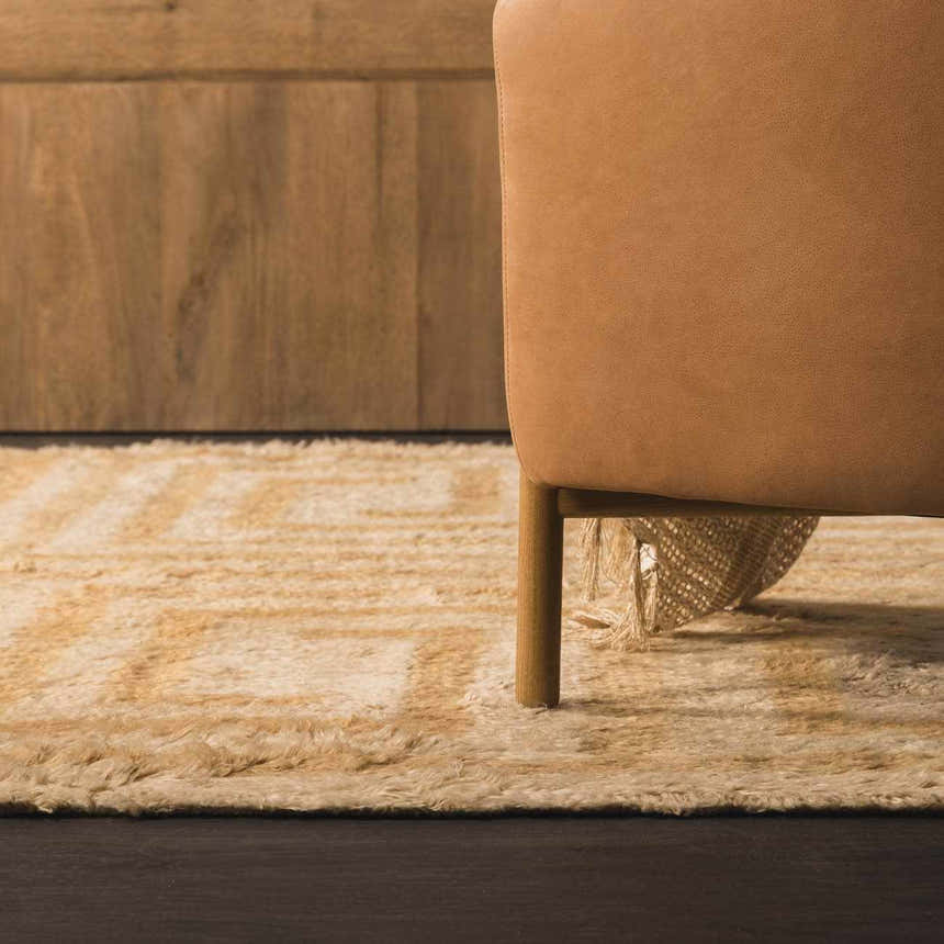 Close-up of the tan and pearl geometric design of the hand-tufted wool Wasim Area Rug next to a camel-colored chair. Styleshot