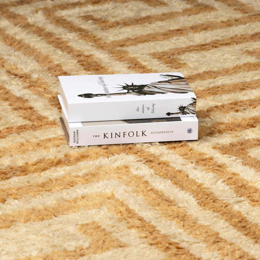 Close-up of the hand-tufted Wasim Area Rug, a wool rug in camel and light wood with a geometric pattern. Styleshot