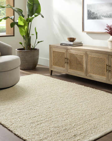 Living room scene with a Teela Cream Area Rug, beige swivel chair, and wood media console. Roomscene-Rectangle
