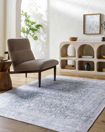 Living room scene with blue Thera Washable Area Rug, gray chair, wood accents, and white textured walls. Roomscene-Rectangle