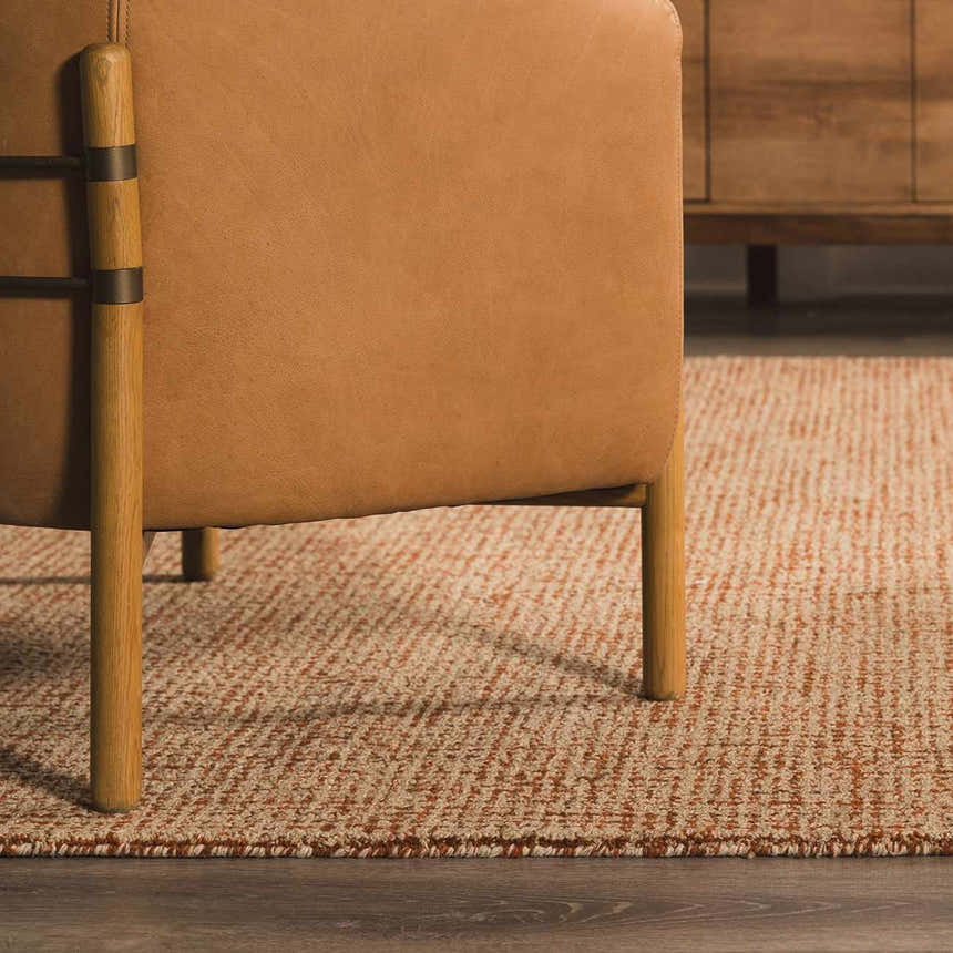 Close-up of Burnt Orange and Ivory Teresita Area Rug under a leather chair in a living room setting. Styleshot