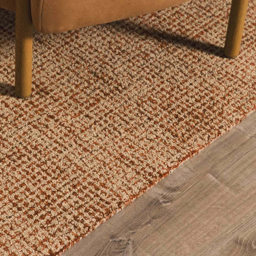 Close-up of Teresita Area Rug showing burnt orange and ivory wool texture under a chair on wood floor. Styleshot