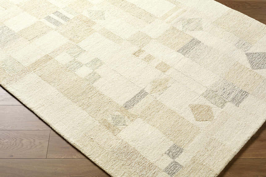 Close-up of the hand-tufted Tovah Area Rug. Ash, light silver, and beige geometric shapes on a textured wool rug. Corner