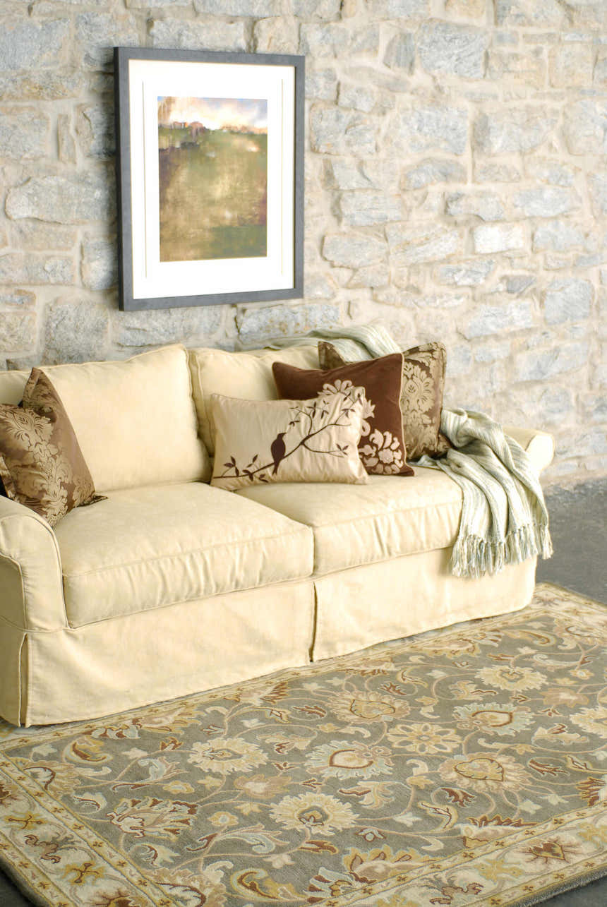 Living room scene with a Cherryfield Hand Tufted Taupe Wool Rug, cream sofa, stone wall, and floral pillows. Roomscene-Rectangle