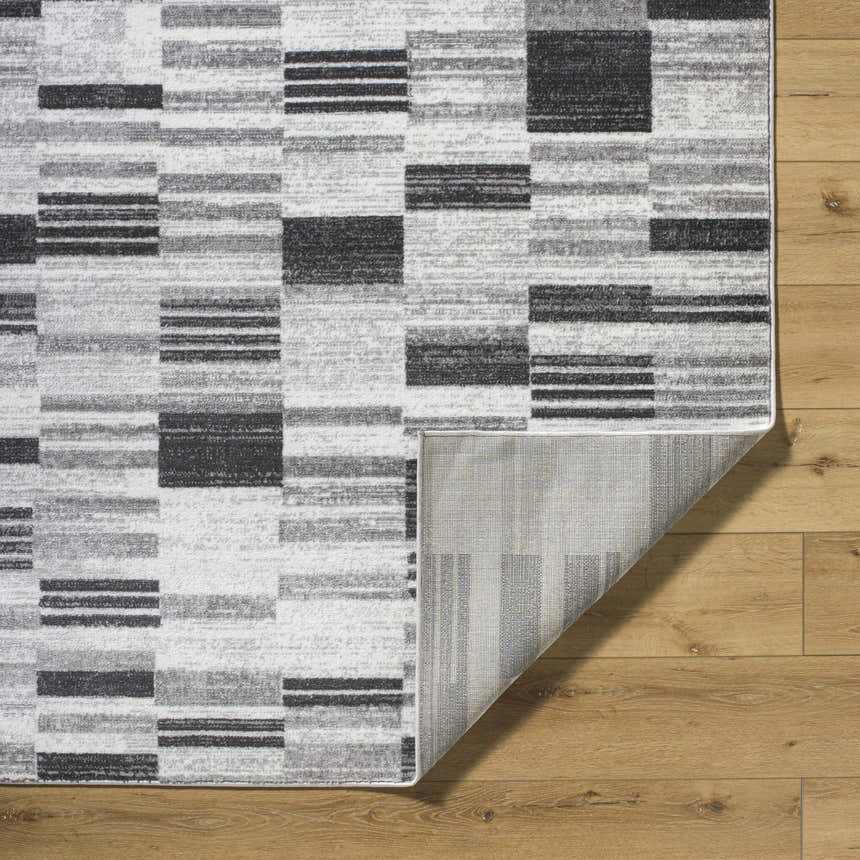 Close-up of the Tehya Gray Area Rug showing its charcoal, silver, and gray geometric block pattern and woven texture. Fold