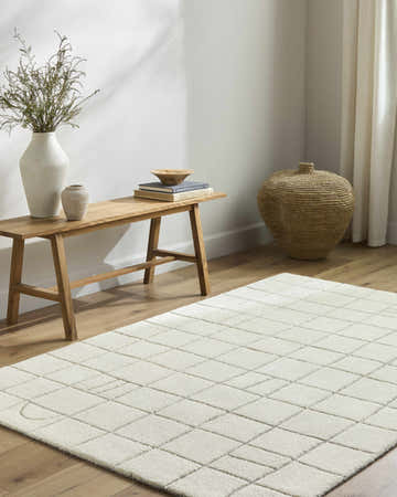 Minimalist living room scene with a beige Tuuka rug, wood bench, vases, and woven basket. Roomscene-Rectangle