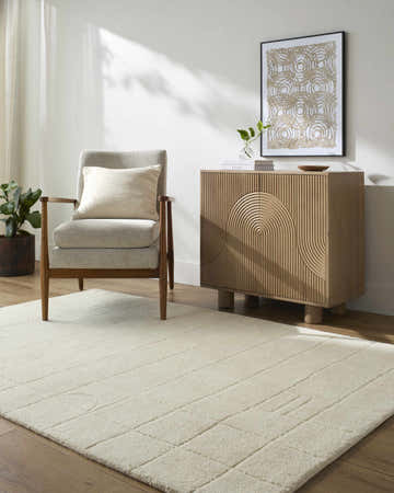 Living room scene with a beige Tuuka Silver Beige Area Rug, gray chair, and wood cabinet. Roomscene-Rectangle