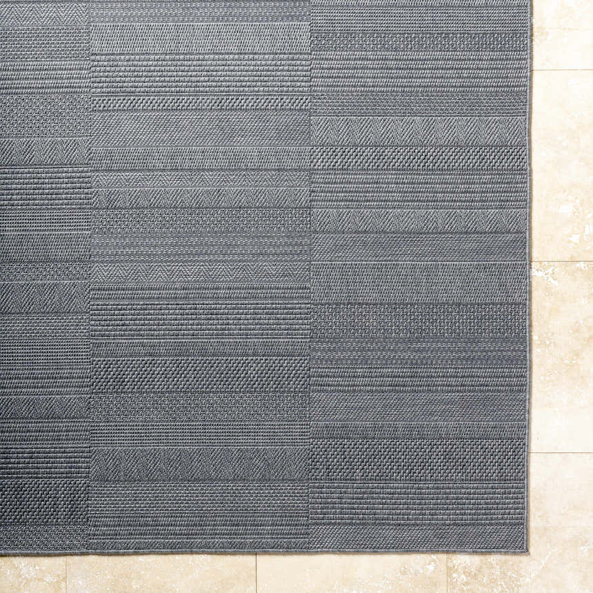 Close-up of the charcoal gray Thana Area Rug featuring a textured, woven, geometric pattern. Corner