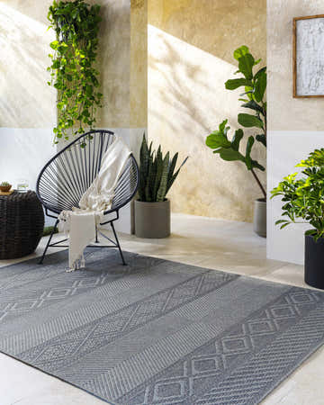 Serene patio scene with gray Aletha Area Rug, modern chair, and lush greenery. Farmhouse style. Roomscene-Rectangle
