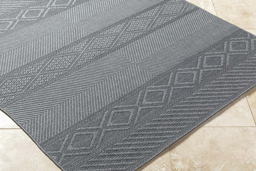 Close-up of the gray Aletha Area Rug showing a geometric diamond and chevron pattern and woven texture. Corner