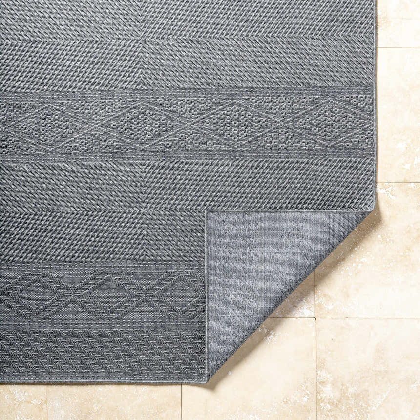 Close-up of the gray Aletha Area Rug showing geometric patterns and textures on a beige tile floor. Fold