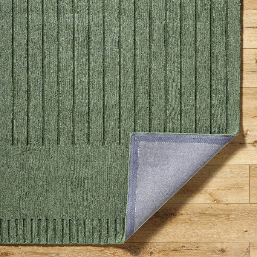 Close-up of the textured Arnona Green Area Rug with vertical stripes on a wood floor, corner flipped to show backing. Fold