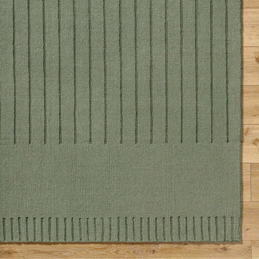 Close-up of the Arnona Green Area Rug showing its ribbed texture and hand-loomed construction on a wood floor. Corner