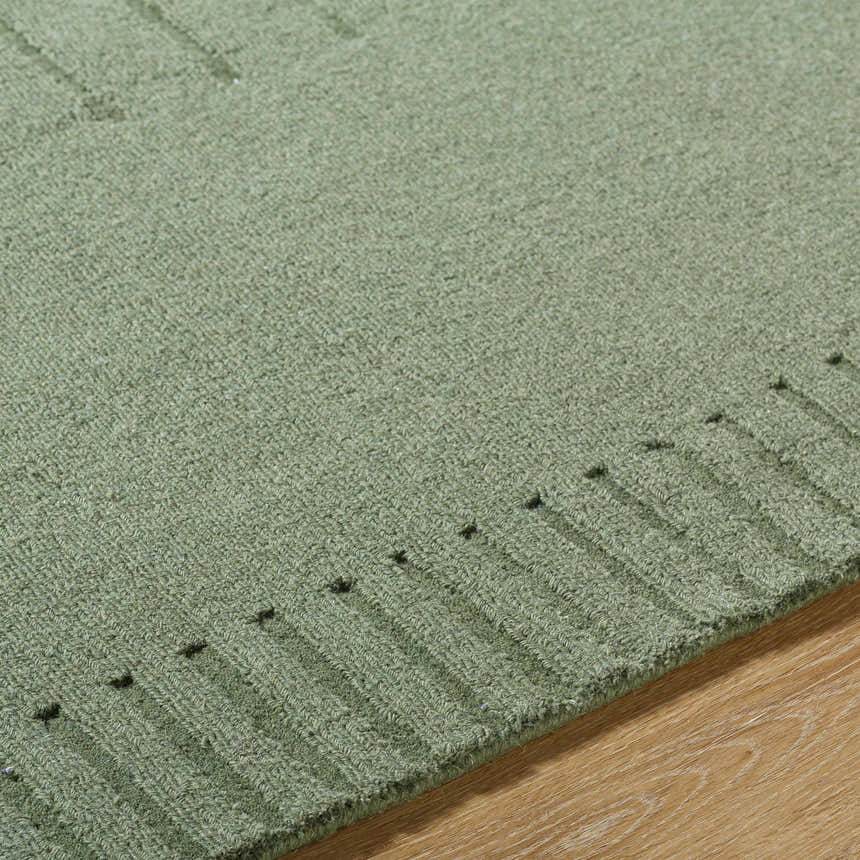 Close-up of the hand-loomed Arnona Green Area Rug showing its texture and subtle geometric pattern on a wood floor. Texture