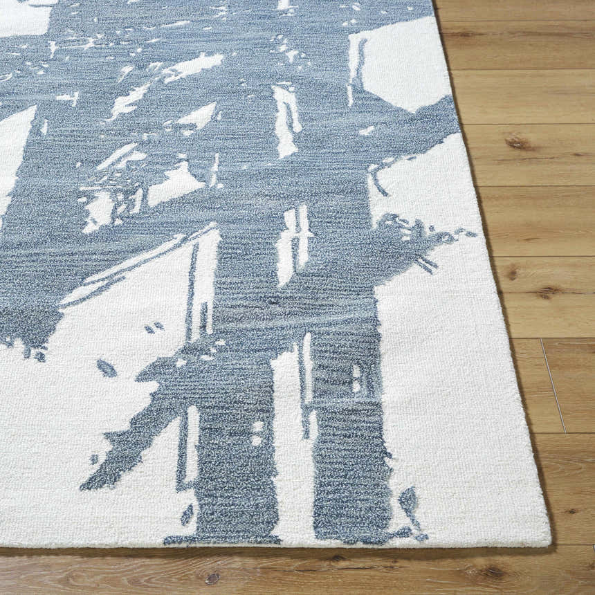 Close-up of Viven Slate Blue Area Rug showing abstract blue pattern on white wool, hand-tufted texture, and wood floor. Front