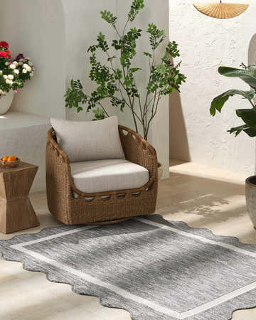 Serene patio scene with a wicker chair on a Varro Charcoal Area Rug. The runner rug has a cream border and farmhouse style. Roomscene-Rectangle