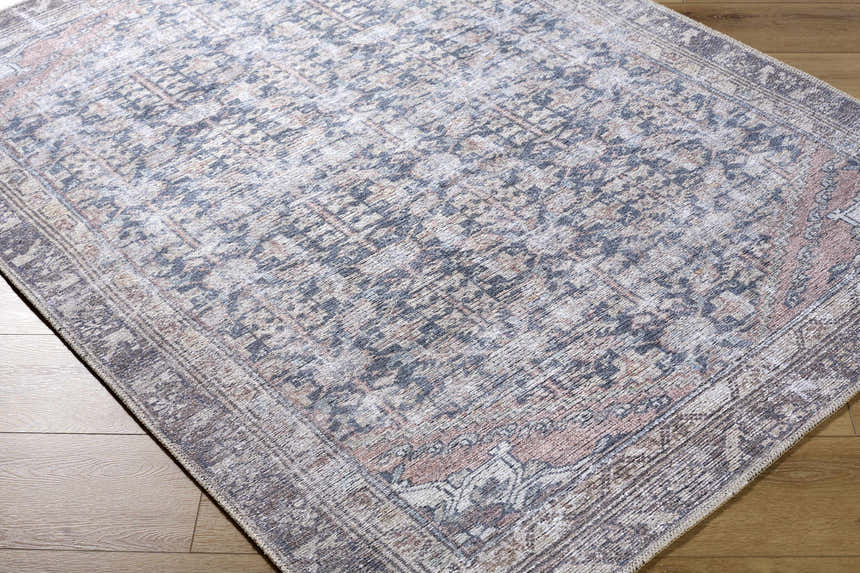 Close-up of the Valar Washable Area Rug. Traditional design in beige, black, blue, and cream on wood floor. Corner