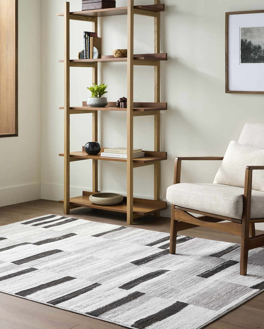 Living room scene with a Vasso Gray Area Rug, wood bookshelf, chair, and neutral tones. Roomscene-Rectangle