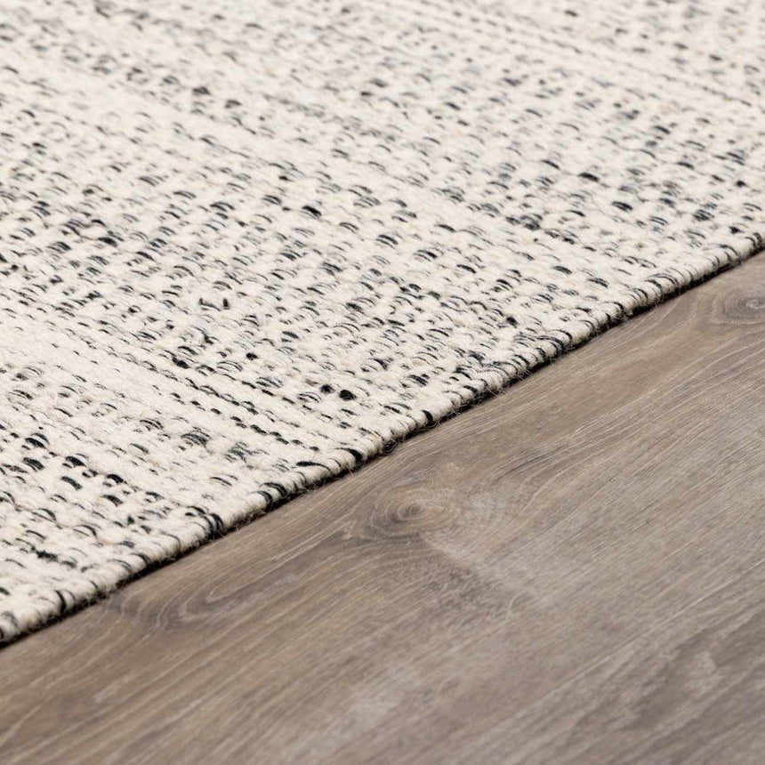 Close-up of the hand-woven Williford Wool Area Rug. Cream rug with black flecks on a wood floor. Transitional style. Corner