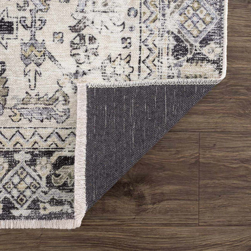Close-up of Holi-4606 washable area rug. Black and gold traditional vintage pattern with a gray backing on dark wood floors. Fold