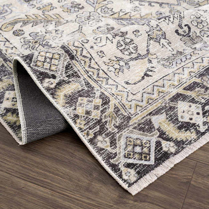 Close-up of the Holi-4606 Washable Area Rug. Black and gold traditional vintage pattern with folded corner showing backing. Fold