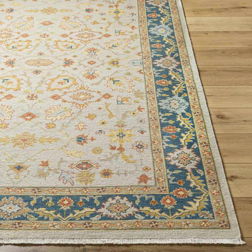 Close-up of the Yenimahalle Premium Rug. Beige rug with burnt orange, ice blue, and mustard floral pattern and teal border. Front