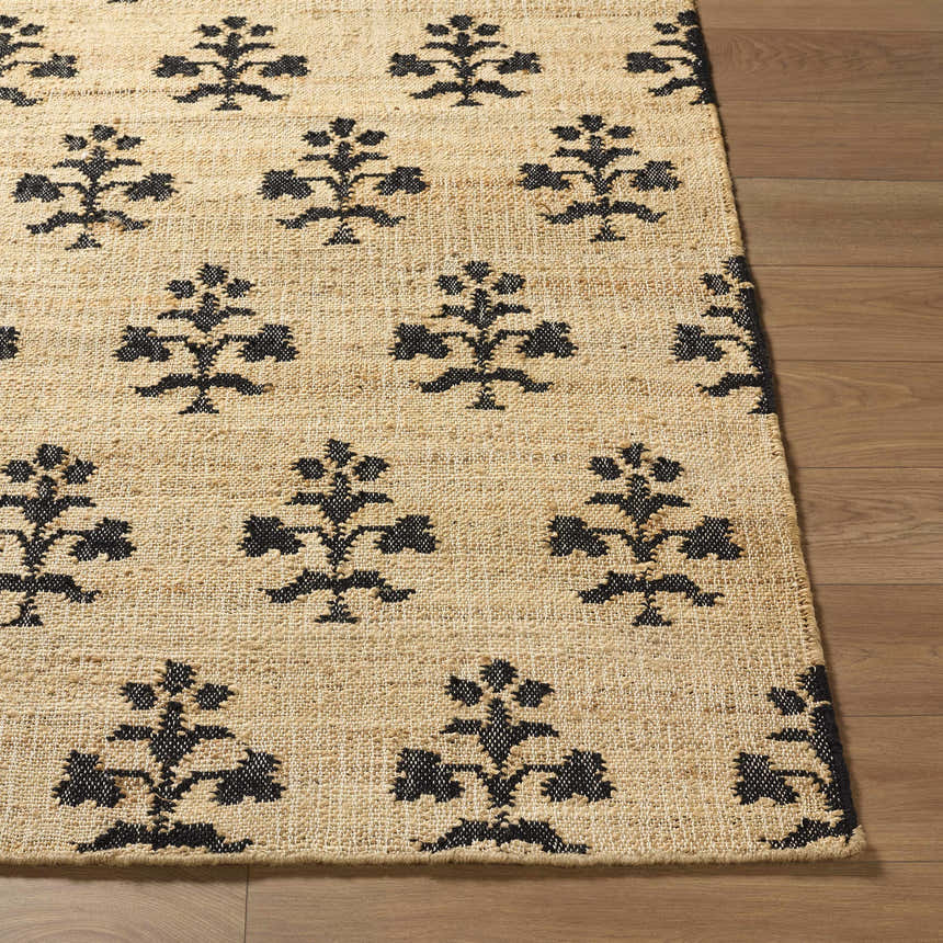 Close-up of the Albina Florentine Jute&Wool Rug. Black floral pattern on a beige, hand-woven jute rug with wood floor. Front