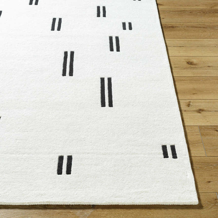 Close-up of the hand-tufted Yitta Ivory Area Rug. Features a contemporary jet black dash pattern on a soft, white wool texture. Front