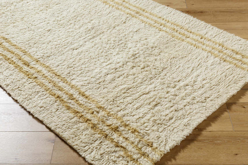 Close-up of the Yahto Area Rug. Hand-tufted wool rug in camel, tan, and pearl with a subtle striped pattern. Corner