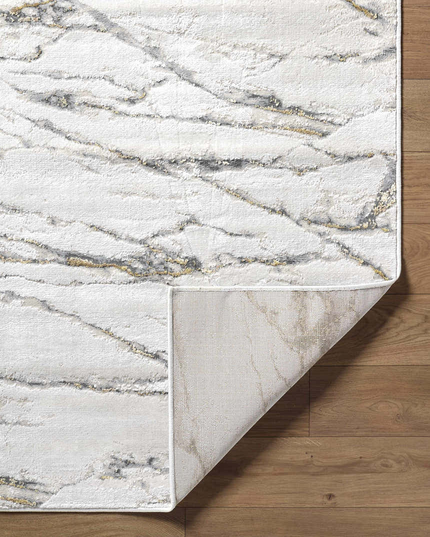 Close-up of the Zelah Area Rug featuring a beige, charcoal, and gold marble-like pattern on a wooden floor. Fold