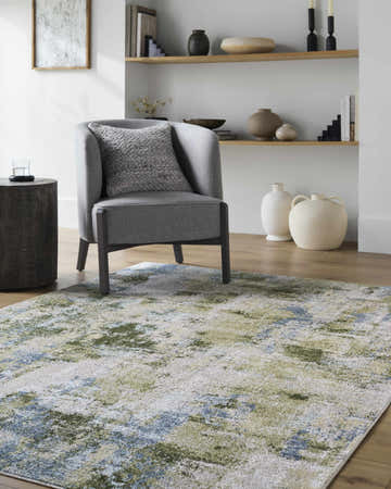 Living room scene with a gray chair on the Anitra Green Washable Area Rug. The rug has green, light brown, and navy tones. Roomscene-Rectangle