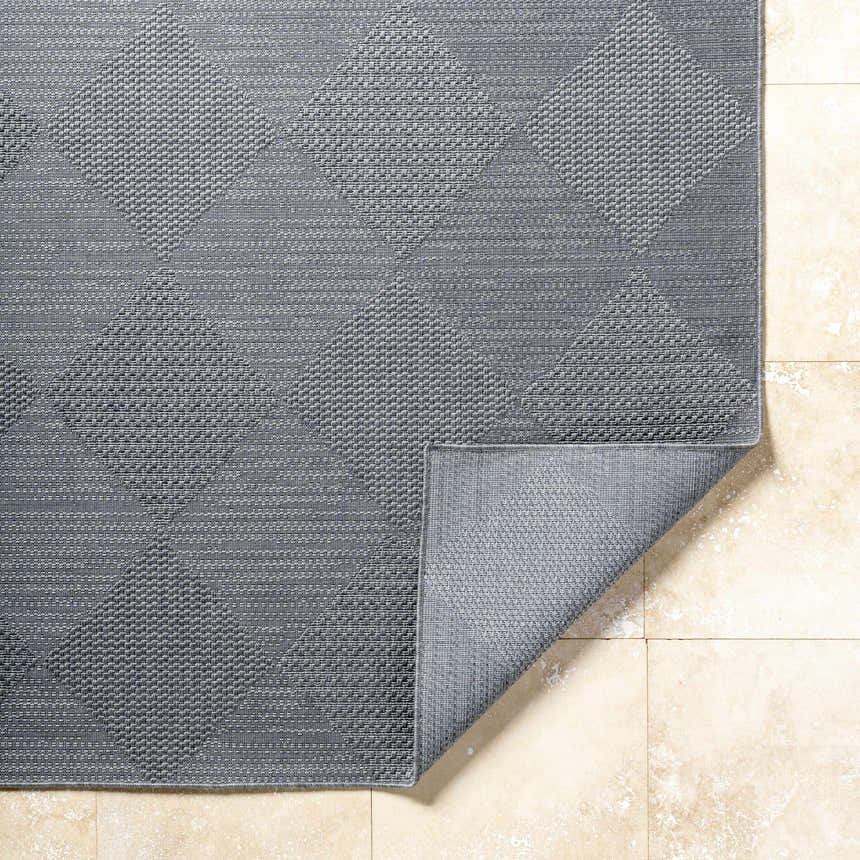 Close-up of the gray Aulani Area Rug showing its woven texture and geometric diamond pattern on a tiled floor. Fold