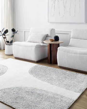 Living room scene with the Zytka Area Rug, featuring a desert sand and silver gray circular pattern. White armchairs and decor. Roomscene-Rectangle