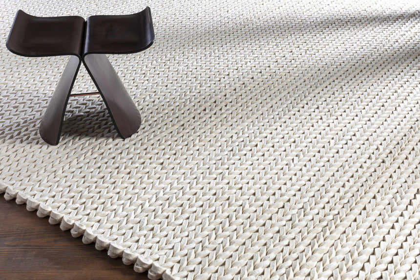 Close-up of the cream Christoval Area Rug showing its hand woven texture and a modern dark wood stool. Styleshot