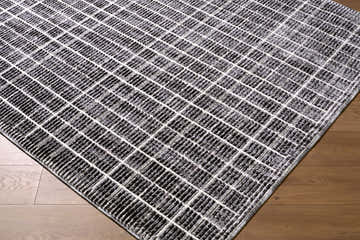 Close-up of Odeon Elle Decor x LIVABLISS EDOD-2302 rug. Black, charcoal, and cream geometric grid pattern on wood floor. Corner